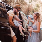 Father carries young child out of vehicle, mother waits outside holding baby. 